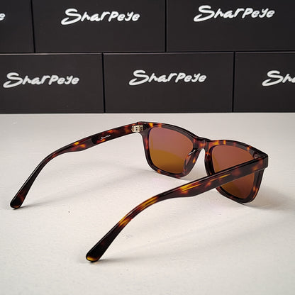 Sunglasses with tortoiseshell frame and brown lenses on a white surface with Sharpeye boxes in the background.