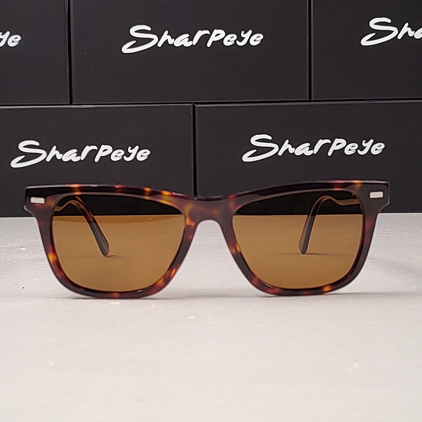 Sunglasses with tortoiseshell frame and brown lenses on a white surface with 'Sharpeye' branding in the background.